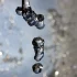 Nahaufnahme von in der Luft gefrorenen Wassertropfen vor einem unscharfen, gräulichen Hintergrund mit Bokeh-Effekt.